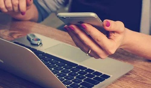 Person holding smartphone while working at laptop with miniature car model on desk